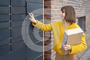 Woman getting parcel from cell of automatic post terminal outdoors