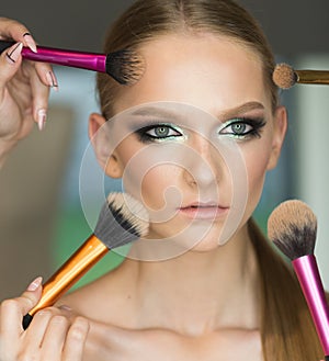 Woman getting powder on skin with brushes, makeup. Hands apply makeup on model face. Woman with young face in beauty