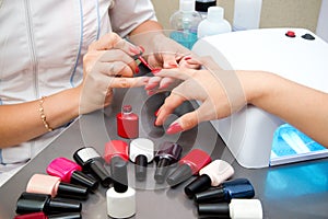 Woman getting professional manicure in beauty salon, master applies gel polish on nails and dry in a uv lamp