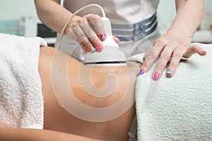 Woman getting ultrasound cavitation treatment by cosmetologist. female client enjoying anti-cellulite procedure at
