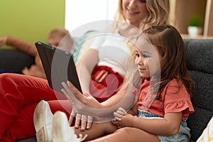 Woman with girl and boy using touchpad sitting on sofa at home