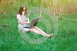 Woman or girl in a dress, with a laptop and headphones, sits on