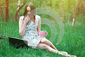 Woman or girl in a dress, with a laptop and headphones, sits on
