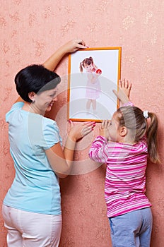 Woman with girl hanging up a picture