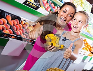 Woman with girl holding thumbs up in grocery shop