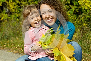 Woman and girl laugh with leaves in garden