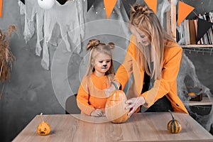 a woman and a girl in make a jack-o-lantern out of large pumpkins for the celebration of halloween. Cut with a knife