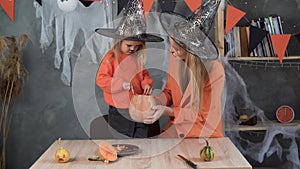 a woman and a girl in make a jack-o-lantern out of large pumpkins for the celebration of halloween. Witch costume, hat