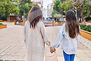 Woman and girl mother and daughter walking with hands together at park