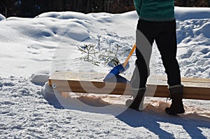 Woman, girl with a plastic baby shovel cleans snow from a wooden bench. he has winter clothes and a slender figure. in the mountai