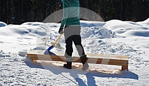 Woman, girl with a plastic baby shovel cleans snow from a wooden bench. he has winter clothes and a slender figure. in the mountai