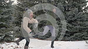 Woman and girl are playing with snowballs in winter forest, beautiful landscape with snowy fir trees