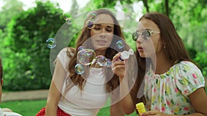 Woman and girl playing with soap bubbles in park. Family laughing outdoors