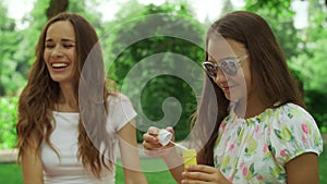 Woman and girl playing with soap bubbles in park. Family laughing outdoors