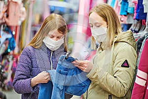 woman and girl in protective mask shopping clothing jeans pants in apparel shop at coronavirus epidemic