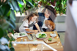 A woman and a girl are seated at a table, enjoying vegetables meal together. Various dishes and utensils are spread out