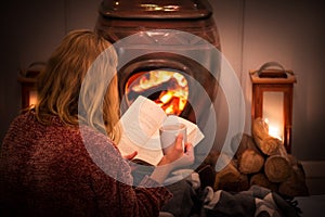 Woman girl sitting in front of a cozy fireplace during winter under a blanket  reading a book drinking coffee/hot chocolate.