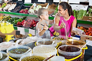 Woman with girl taking pickled olives from bucket