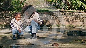 Woman girl watching reptile in sunny park. African family enjoying wildlife.