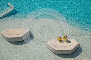 Woman and girl wear weave hat and sit relax on white sofa in pool.