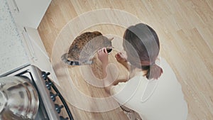 Woman gives a bowl of food to cat at home.