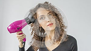 Woman gives herself a curly hairstyle. Hair care concept. A curly woman dries her hair at home with a hair dryer with a