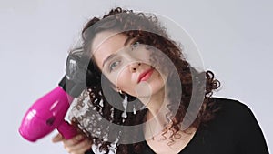 Woman gives herself a curly hairstyle. Hair care concept. A curly woman dries her hair at home with a hair dryer with a