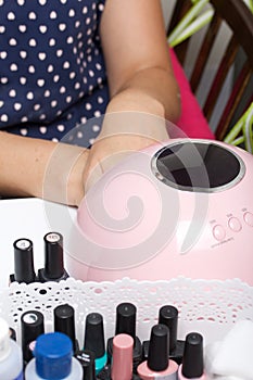 A woman gives herself a manicure. Dries the varnish in a UV lamp. Next to the nail Polish in bottles