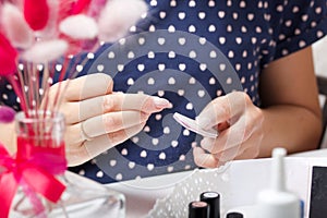 A woman gives herself a manicure. Removes old nail Polish with a nail buff. Next to a set of lacquers, tools and a bouquet of photo