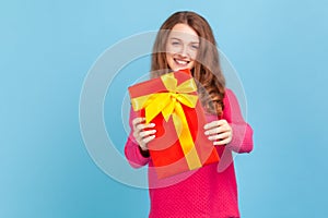 Woman giving gift box to camera with excited smile, greeting on holiday and sharing present.