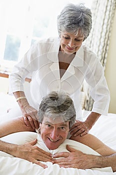 Woman giving man massage in bedroom smiling