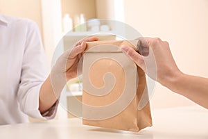 Woman giving paper bag with order to customer in shop, closeup.