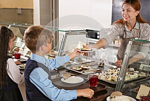 Woman giving plate with healthy food to boy in canteen