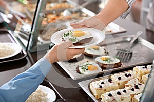 Woman giving plate with healthy food to boy in school canteen