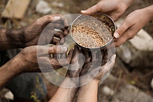 Woman giving poor homeless people bowl of wheat outdoors