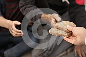 Woman giving poor homeless people pieces of bread outdoors