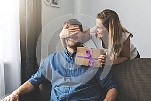 Woman giving surprise gift to beloved man at home. closed eyes with hand from behind