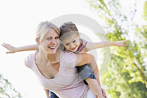 Woman giving young girl piggyback ride smiling
