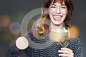 Woman with a glass of champagne on dark background,flares and bokeh. Lady with long curly hair and ref lips celebrating and laughi photo