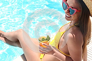 Woman with glass of drink near swimming pool, closeup