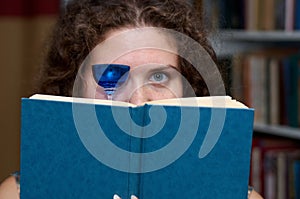 A woman with a glass in her hands on the background of a bookcase reads a book
