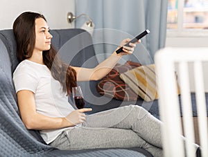 Woman with glass of red wine watching tv at home