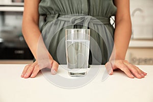 Woman with glass of water at table in kitchen