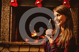 Woman with a glass of wine by the fireplace. Young attractive wo