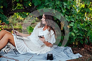 woman with a glass of wine and a laptop in the vineyard