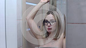 Woman with glasses in front of a mirror combing her hair