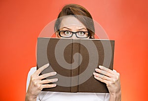 Woman with glasses hiding face behind book