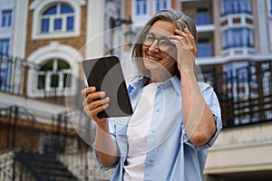 Woman in Glasses Holding Tablet in Front of Building