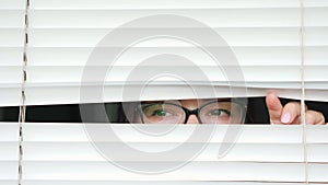 Woman with glasses looking at someone through white blinds