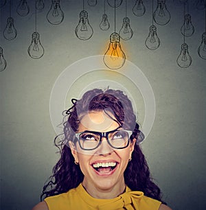 Woman in glasses looking up at idea light bulb above head